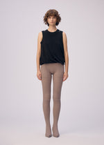 A person with short curly hair stands against a plain background, wearing the ISSEY MIYAKE DRAPE JERSEY-66 sleeveless top and taupe ribbed tights. They face forward with a neutral expression and arms relaxed at their sides.