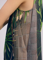 The ISSEY MIYAKE URBAN JUNGLE JERSEY is a sleeveless top with a green bamboo print on a gray grid background, shown in close-up to highlight the design and the wearer’s bare upper arm.