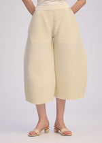 A person models ISSEY MIYAKE's CORRUGATED KNIT wide-leg, cream cropped pants with open-toed heeled sandals. The photo is waist-to-ankle cropped, set against a simple light background.
