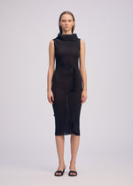 A woman with straight hair wears ISSEY MIYAKE’s ADVENTITIOUS：HIGH-NECKS sleeveless knit dress, featuring a high asymmetric collar and unique waist detailing, styled simply with black sandals against a plain light background.