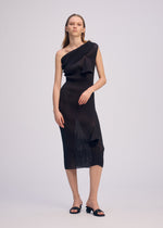 A woman in the ISSEY MIYAKE ADVENTITIOUS: HIGH-NECKS black ribbed midi dress with sculptural details and black open-toe sandals stands against a light gray background, emphasizing its unique organic cotton design.