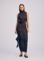 A woman models the ISSEY MIYAKE ADVENTITIOUS: SLEEVES sleeveless, sheer black knit dress with an asymmetrical hem and scarf-like detail against a plain background, styled with black open-toe sandals.