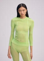 A person with long dark hair wears the ISSEY MIYAKE SLITS MESH AP, a sheer neon green knit top and pants perfect for layering, standing against a plain light background and gazing at the camera with a neutral expression.