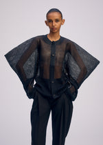 A person models the ISSEY MIYAKE CIALDA—a sheer black mesh-like wide-sleeved button-up top—over black pants, posing confidently with hands in pockets against a light background.