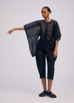 Against a plain background, a person with short, slicked-back hair and a neutral expression wears ISSEY MIYAKE's CIALDA: a sheer black mesh-like top with wide sleeves, paired with black cropped pants and black shoes.