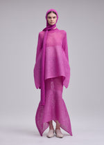 A person stands against a plain background wearing the ISSEY MIYAKE PANINI BALACLAVA in bright pink wool-alpaca knit, plus a matching long top, skirt, and scarf, paired with light-colored shoes.