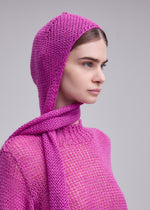 A person in profile with a neutral expression wears the ISSEY MIYAKE PANINI BALACLAVA, bright pink wool-alpaca, and matching scarf against a plain gray background.