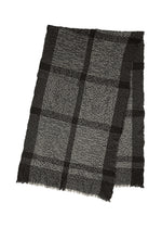 The BUMPY WOOL STOLE by ISSEY MIYAKE, a black and gray cashmere-blend accessory with a plaid pattern, subtly bumpy texture, and fringed edges, is laid flat on a white background.