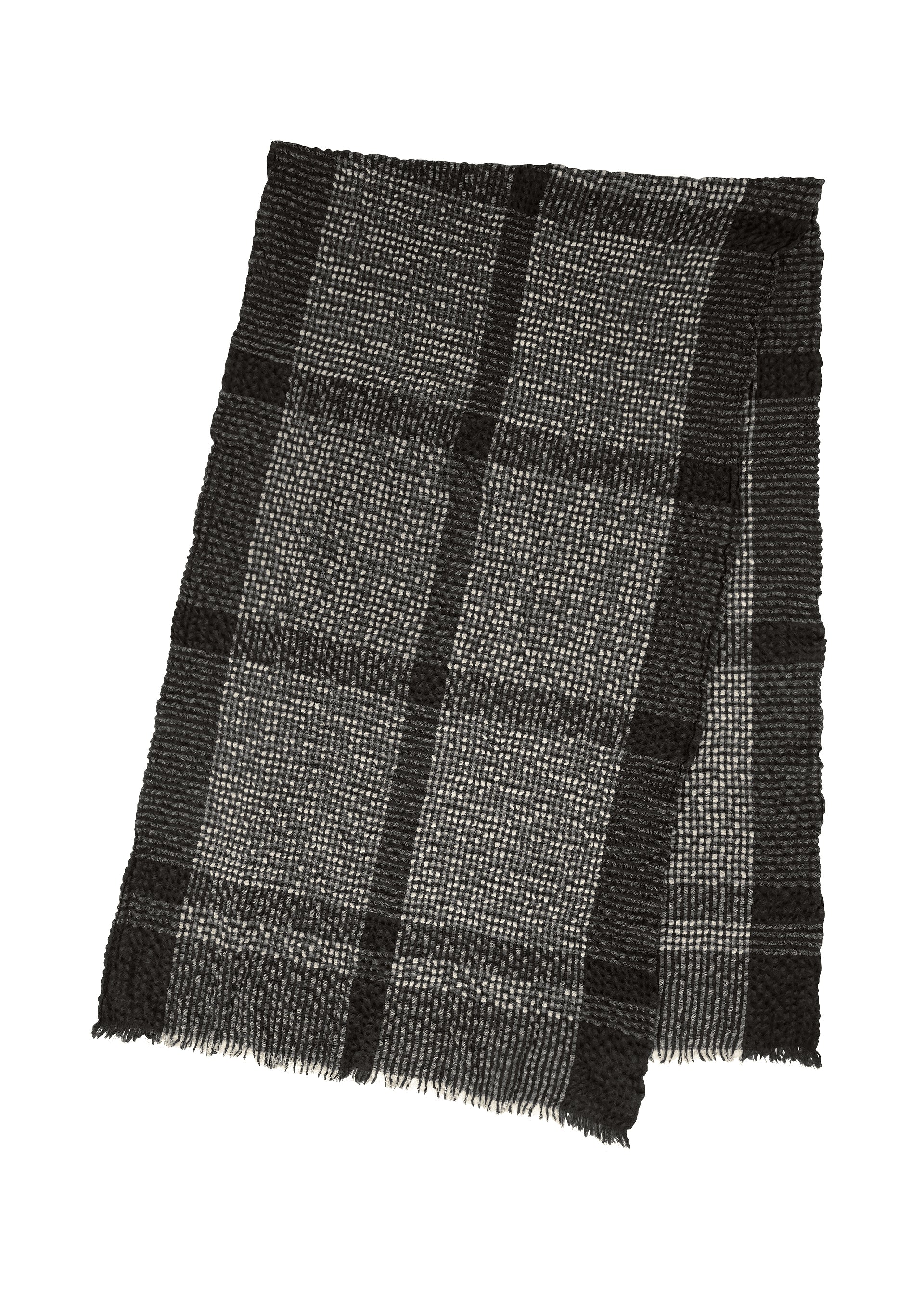Zoomed view The BUMPY WOOL STOLE by ISSEY MIYAKE, a black and gray cashmere-blend accessory with a plaid pattern, subtly bumpy texture, and fringed edges, is laid flat on a white background.