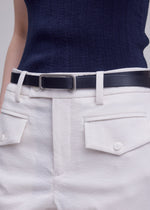 A person wears a textured navy sleeveless top tucked into high-waisted white trousers with two buttoned front pockets, styled with the SOLID LEATHER BELT by ISSEY MIYAKE. The cropped image displays only their torso and upper legs.