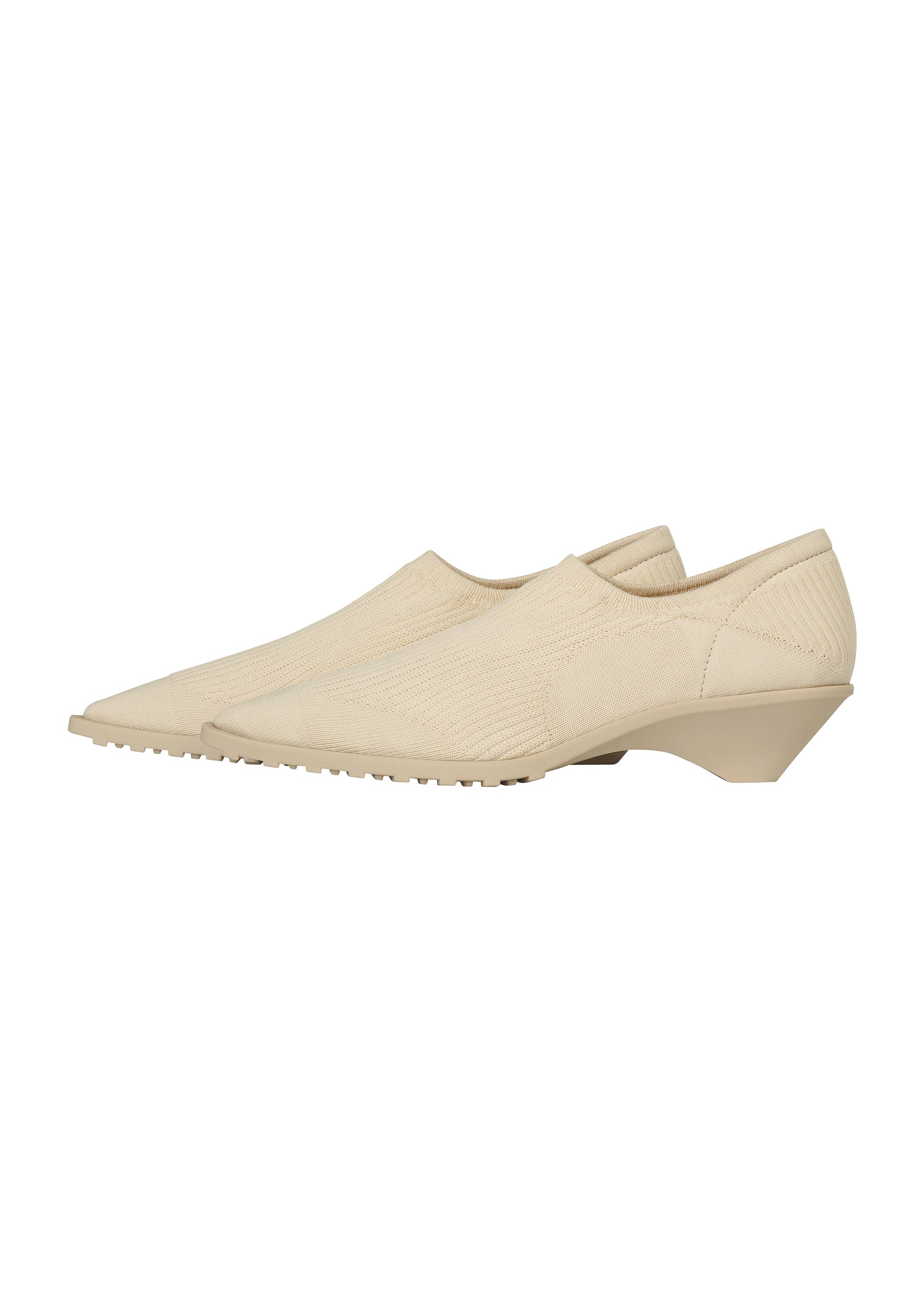 Zoomed view A pair of beige, pointed-toe slip-on shoes with low, angular heels and textured uppers, inspired by ISSEY MIYAKE ANNA’s signature sock-like design, shown on a white background.
