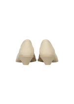 Back view of a pair of beige, low-heeled, closed-toe ISSEY MIYAKE ANNA shoes with a textured fabric upper reminiscent of knitted footwear, set against a plain white background.