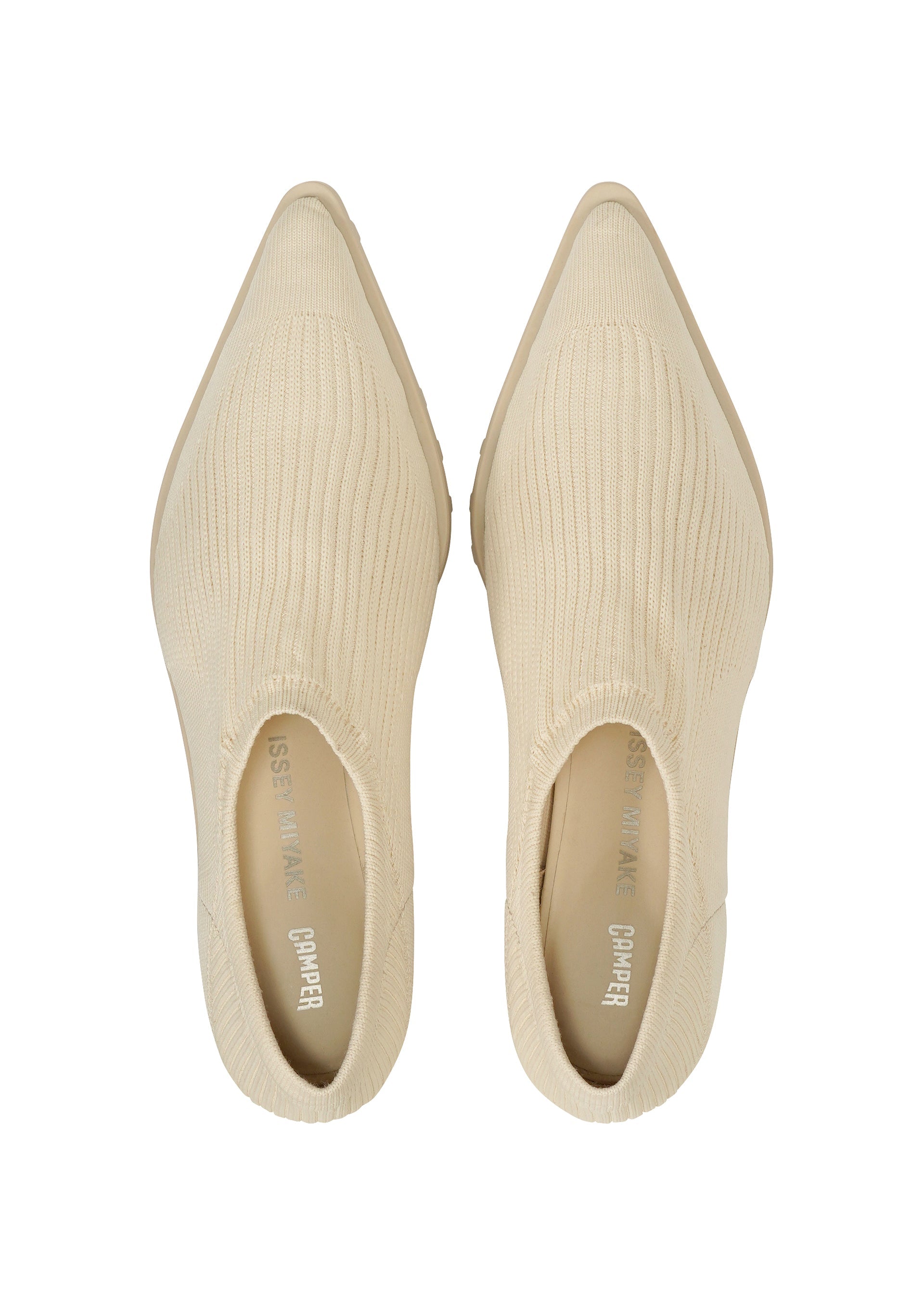 Zoomed view A pair of ANNA cream-colored, ribbed knit slip-on shoes by ISSEY MIYAKE, featuring pointed toes and a sock-like silhouette, viewed from above on a white background.