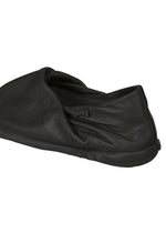 A PEU FORM black leather shoe cover by ISSEY MIYAKE, featuring a soft, wrinkled texture characteristic of the brand’s unique design sensibility, lies flat on a white background.