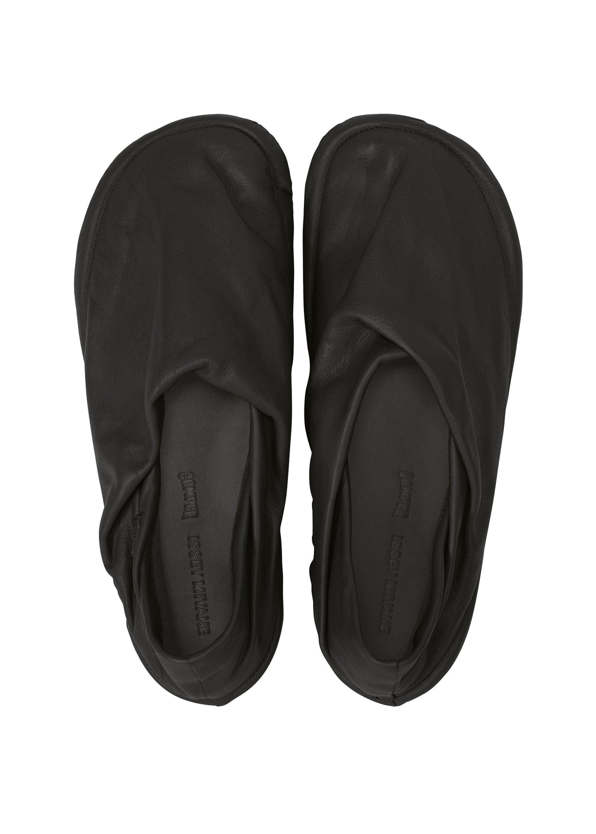 Zoomed view A pair of black PEU FORM slippers by ISSEY MIYAKE, crafted from soft leather with rounded toes, are shown from above against a white background. Their simple, unembellished design reflects the minimalistic style synonymous with the brand.