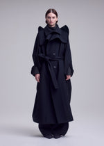 A person stands facing forward, wearing an oversized black premium wool coat with a belt, wide lapels, and long sleeves, paired with loose black pants from the ISSEY MIYAKE CALLIGRAPH collection (Autumn Winter 2026/27), set against a plain light gray background.