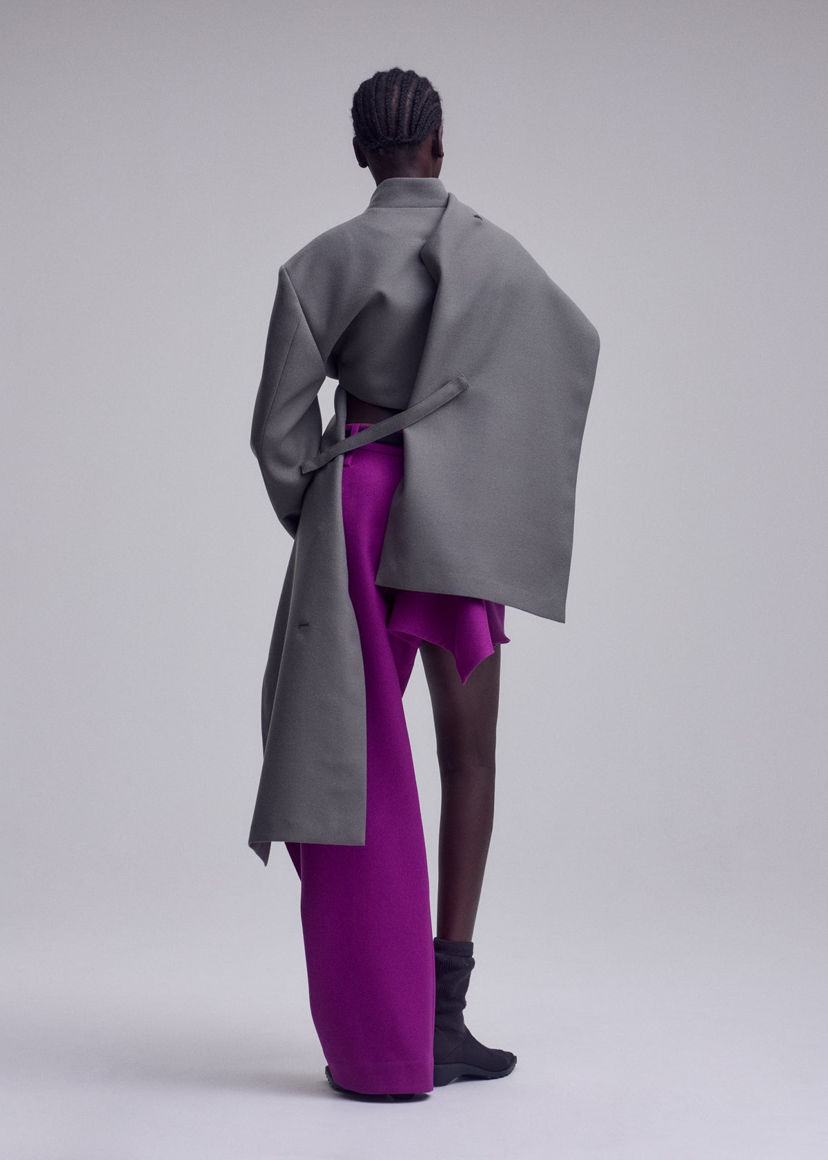 A person stands facing away, dressed in the ISSEY MIYAKE CALLIGRAPH premium wool jacket crafted from woven nashiji pebbled fabric with exaggerated sleeves, paired with bright magenta wide-leg pants and skirt and black ankle boots against a plain background—a striking look from the ISSEY MIYAKE Autumn Winter Collection. view 6 of 8