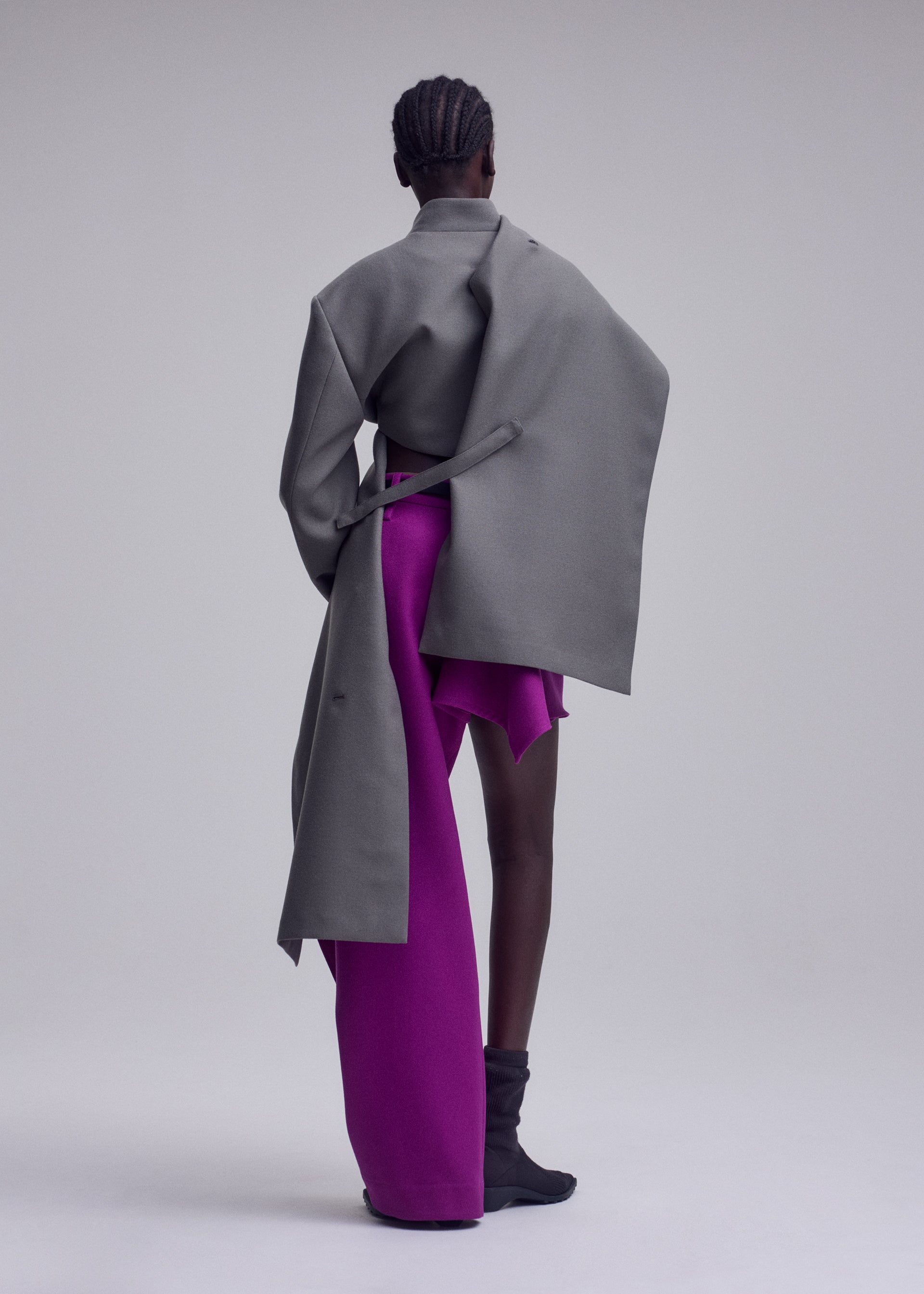 Zoomed view A person stands facing away, dressed in the ISSEY MIYAKE CALLIGRAPH premium wool jacket crafted from woven nashiji pebbled fabric with exaggerated sleeves, paired with bright magenta wide-leg pants and skirt and black ankle boots against a plain background—a striking look from the ISSEY MIYAKE Autumn Winter Collection.