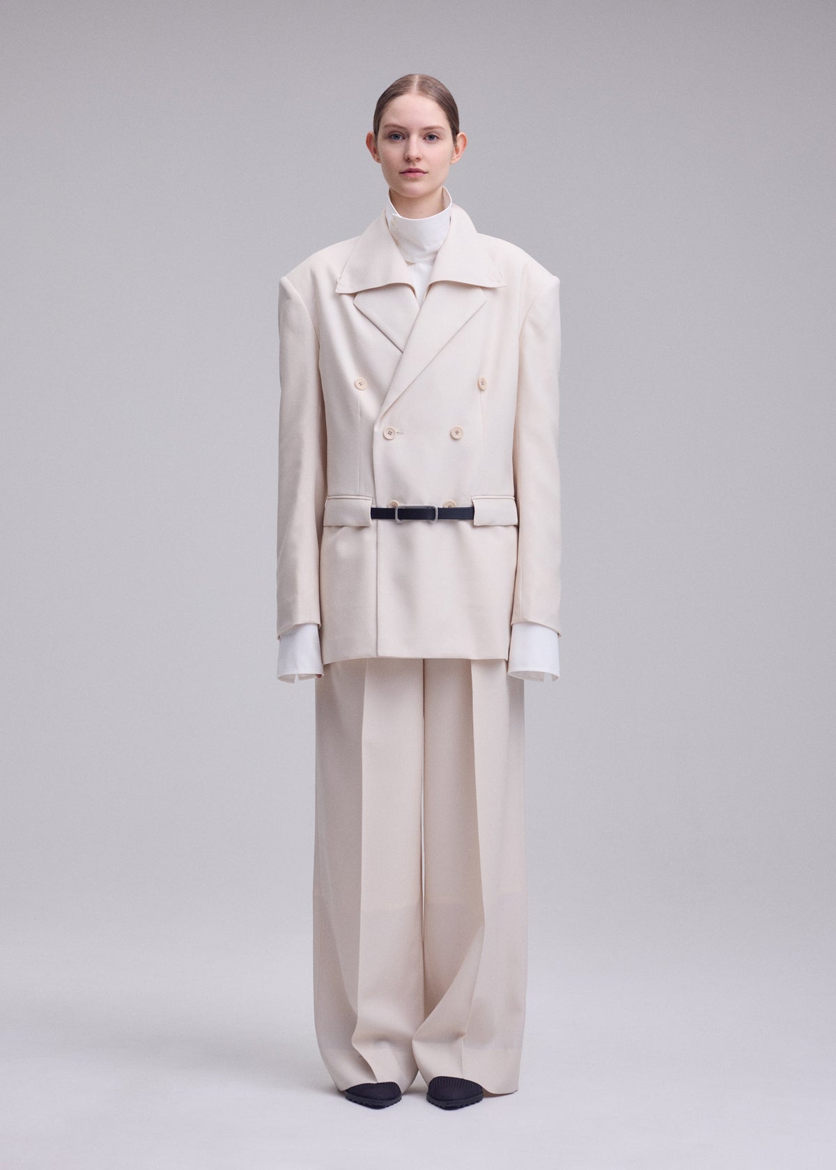 A person stands facing forward in an oversized cream suit with wool wide pants, a double-breasted blazer, and white turtleneck, embodying ISSEY MIYAKE’s style. The look features UNTITLED by ISSEY MIYAKE on a light gray background. view 4 of 6