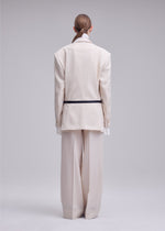 A person with long hair tied back wears ISSEY MIYAKE’s UNTITLED off-white SUPER120’s wool suit with wide pants and a striped jacket, standing with their back to the camera against a plain background.