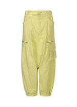 The GRAINY PANTS by ISSEY MIYAKE are loose-fitting, pale yellow sarouel cargo pants with large side pockets, a flap pocket on one leg, button and zipper closure, and cropped legs gathered at the hems, shown against a white background.