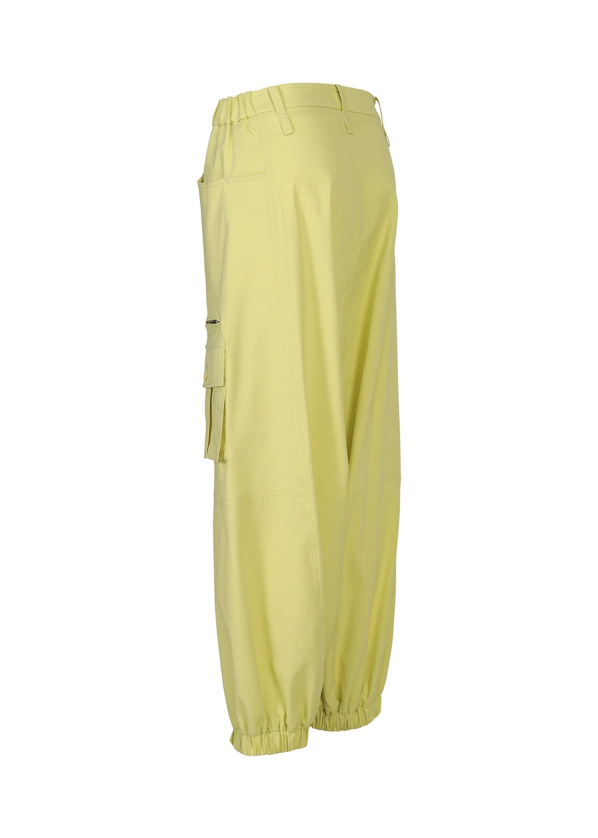The GRAINY PANTS by ISSEY MIYAKE are light yellow stretch cotton sarouel pants with an elastic waistband, ankle cuffs, side pockets, and a zippered flap pocket on the left leg, shown from the side against a white background. view 5 of 8