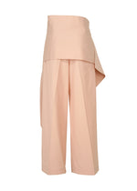The LUSTROUS WOOL PANTS by ISSEY MIYAKE are wide-legged, high-waisted peach gabardine trousers featuring an overlapping, asymmetrical waistband detail and front pleats. Expertly crafted from a wrinkle-resistant wool blend, the pants are showcased against a white background.