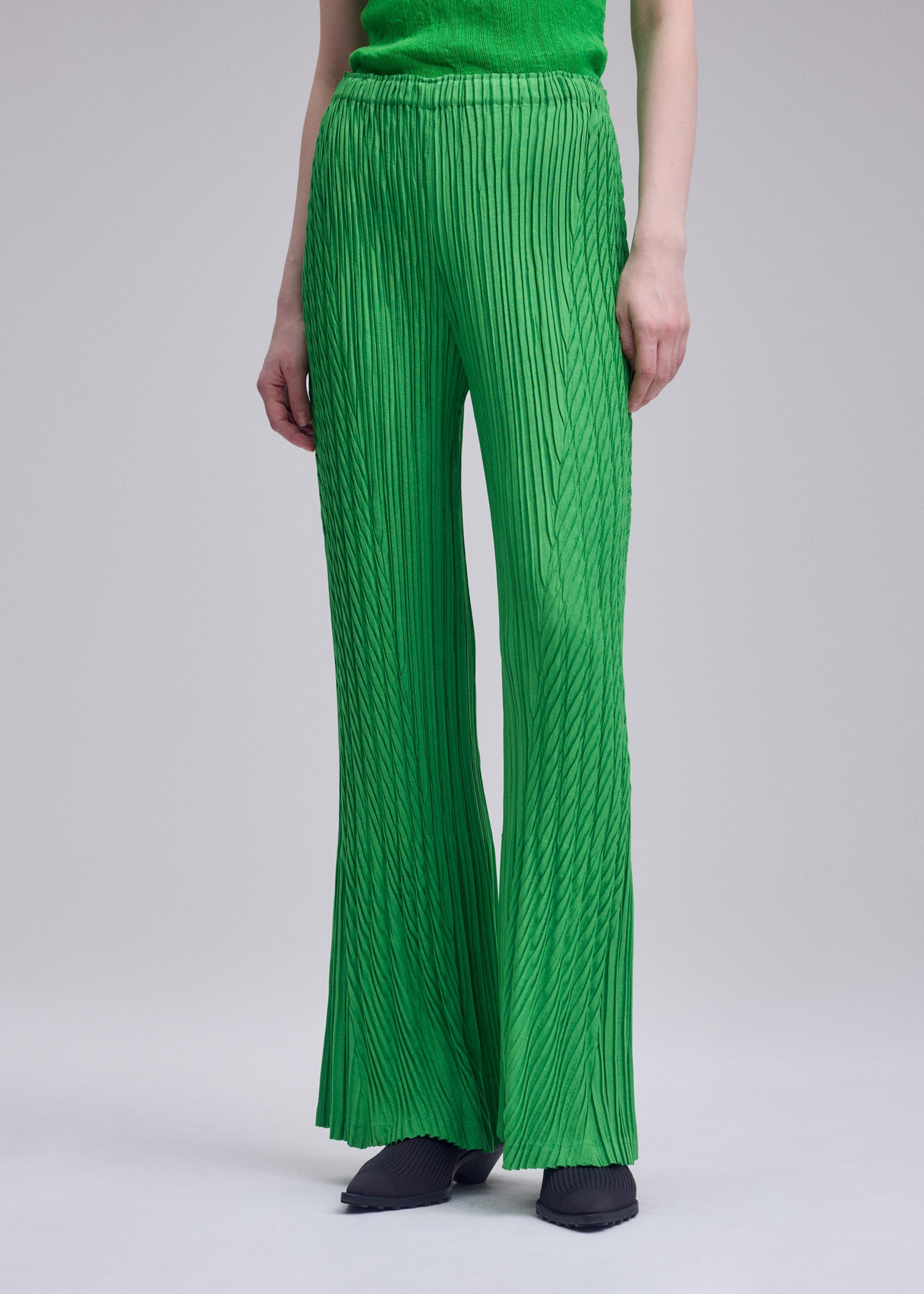 Zoomed view A person wearing ISSEY MIYAKE's UNFURLING PLEATS wide-leg pants and a matching green top, paired with black pointed shoes; the photo is cropped below the shoulders against a plain background.