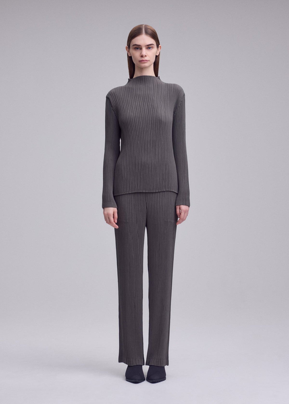 A person faces forward in the ISSEY MIYAKE HATCHING PLEATS ribbed gray long-sleeve top and pleated straight pants set, paired with black shoes against a plain light gray background. view 5 of 7