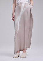 A person wearing a white top, cream-colored shoes, and the ISSEY MIYAKE HANDS OF LOVER PLEATS skirt—a light beige pleated maxi with an original pattern—stands against a plain gray background, their hands relaxed by their sides.