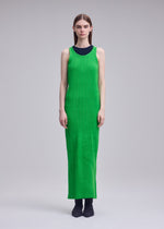 A person faces forward wearing ISSEY MIYAKE's RILL, an ankle-length sleeveless bright green pleated dress over a black top with dark shoes. The subtly textured garment stands out against a plain light gray background.