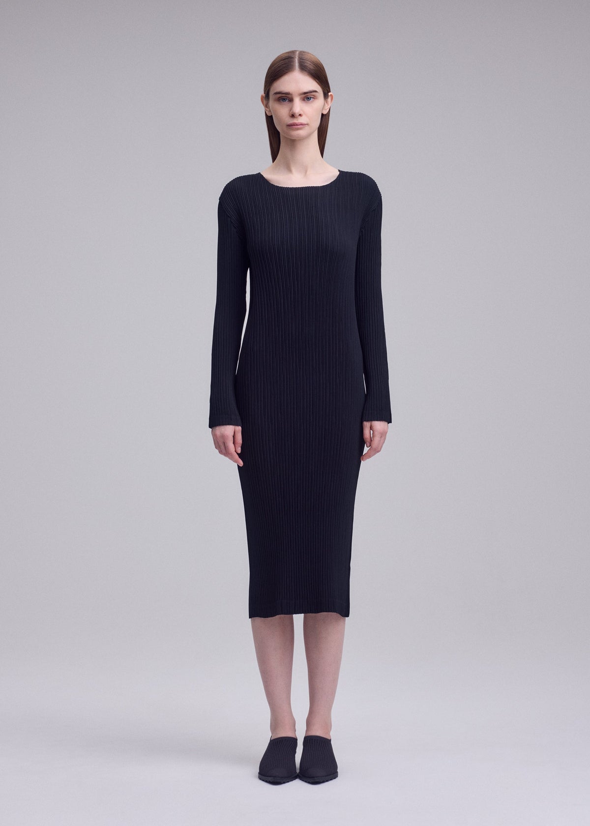 Zoomed view A person stands facing forward against a gray background, wearing the ISSEY MIYAKE HATCHING PLEATS long-sleeved black ribbed pleated dress with black shoes.