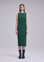 A person stands facing forward in the ISSEY MIYAKE RHOMBUS PLEATS, a sleeveless green dress with a relaxed fit and knee-length hem, paired with black socks and shoes, against a plain gray background.