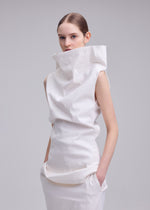 A woman with slicked-back hair wears the ISSEY MIYAKE ALLOW dress—a modern, sculptural white piece in washi paper-blend fabric with a high, structured collar and pockets—standing against a plain light grey background.