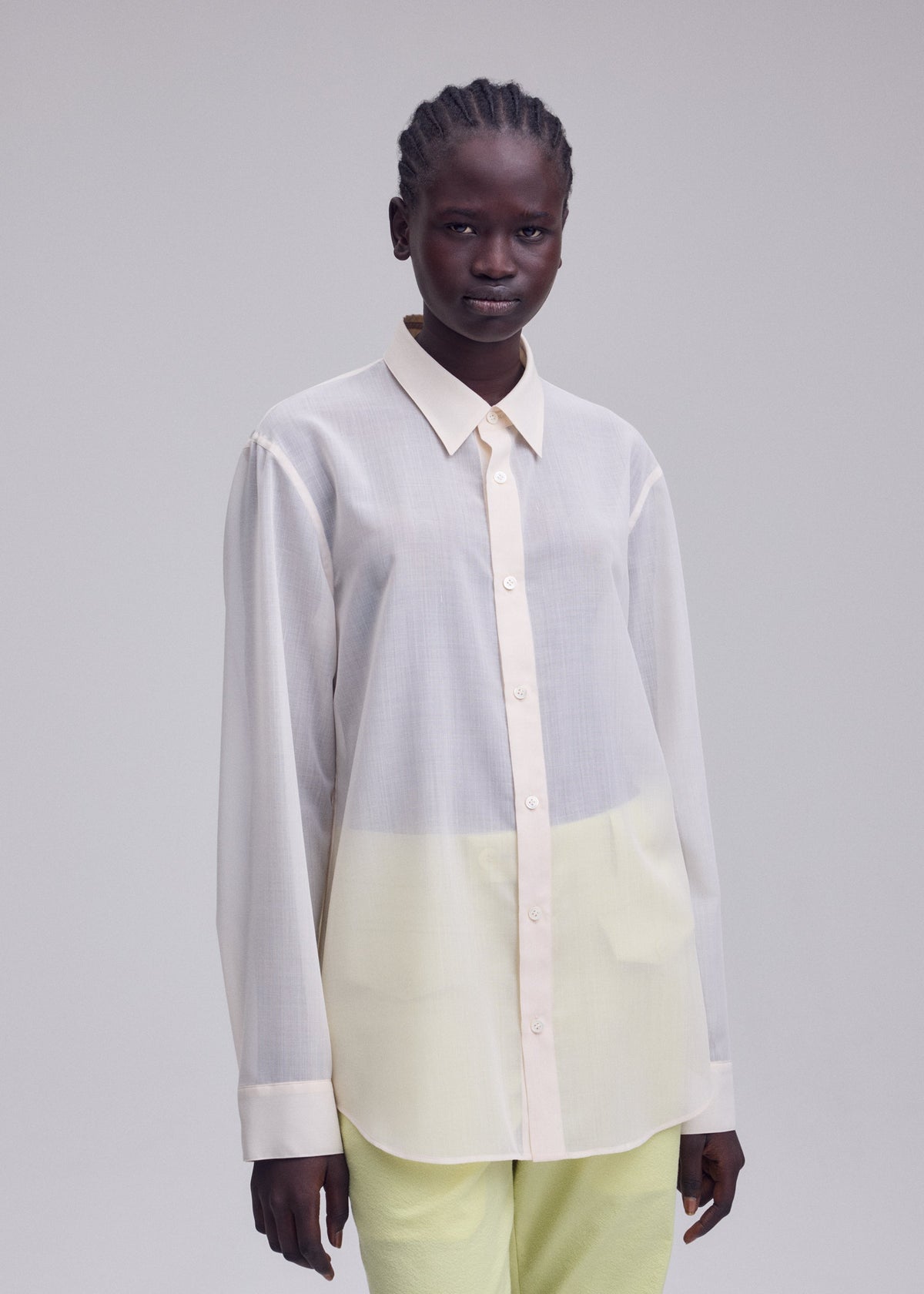 A person stands against a plain background, wearing the ISSEY MIYAKE SHEER WOOL shirt with a subtle gradient and light yellow pants, gazing directly at the camera with a neutral expression. view 7 of 7