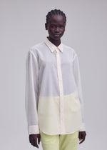 A person stands against a plain background, wearing the ISSEY MIYAKE SHEER WOOL shirt with a subtle gradient and light yellow pants, gazing directly at the camera with a neutral expression.