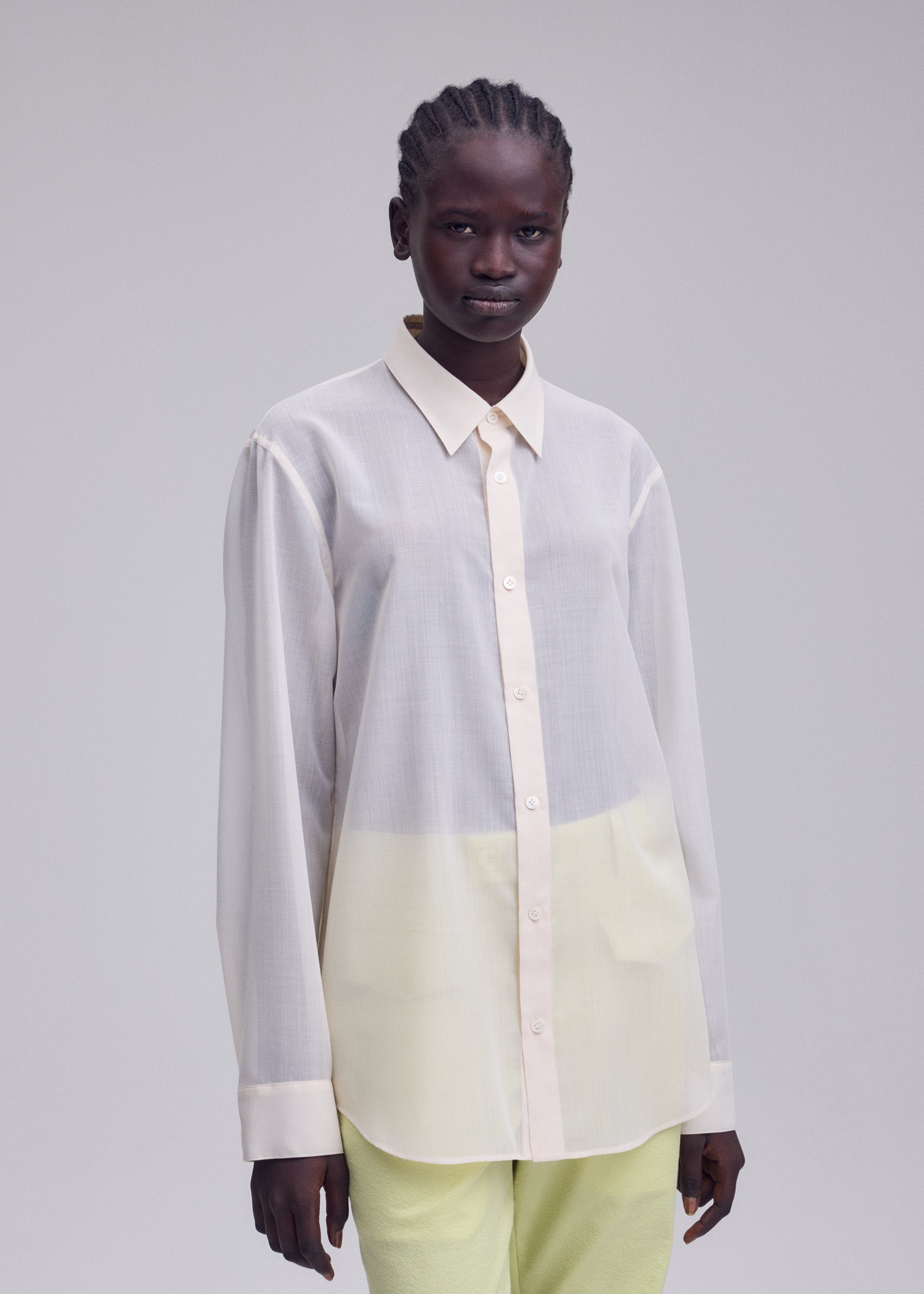 Zoomed view A person stands against a plain background, wearing the ISSEY MIYAKE SHEER WOOL shirt with a subtle gradient and light yellow pants, gazing directly at the camera with a neutral expression.