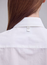 Close-up of the back of a person wearing the MONSIEUR SHIRT by ISSEY MIYAKE, featuring a regular collar and crafted from high-twist cotton, with straight brown hair partially visible and a button detail on the back of the collar.