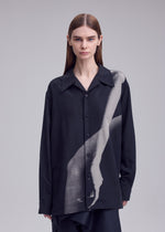 A person with straight brown hair wears the ISSEY MIYAKE HANDS OF LOVER shirt—an open-collar black poplin piece adorned with a grayscale print of an arm and hand across the front—standing against a light gray background.