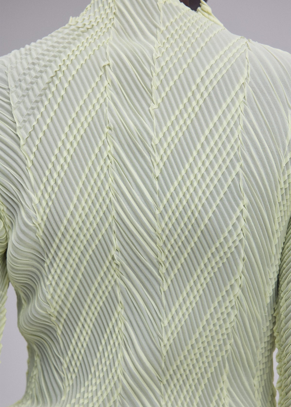 Close-up of the back of the ISSEY MIYAKE ZIGZAG PLEATS top, crafted from light green fabric with structured folds forming a geometric, chevron-inspired pattern and finished with a signature zigzag hem. view 8 of 8