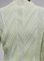 Close-up of the back of the ISSEY MIYAKE ZIGZAG PLEATS top, crafted from light green fabric with structured folds forming a geometric, chevron-inspired pattern and finished with a signature zigzag hem.