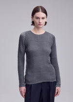 A person with short brown hair wears the ISSEY MIYAKE SUEDE LIKE PLEATS textured gray long-sleeve shirt and black pants, standing against a plain light gray background.