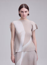 A person with short brown hair wears the ISSEY MIYAKE HANDS OF LOVER PLEATS set— a beige, pleated top and skirt crafted from polyester crepe de chine featuring subtle white patterns inspired by monochrome film motifs—standing against a plain light background.