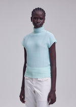A person with short braided hair models the ISSEY MIYAKE WOOLY PLEATS-68, a light blue stretchy high-neck top with French sleeves, paired with off-white pants against a plain light gray background.