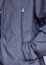 Close-up of a person wearing the ISSEY MIYAKE REFLECTION jacket—a textured gray piece with a diagonal zipper and right hand tucked into a side pocket—featuring subtle reflector fabric that enhances both style and visibility.