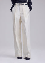 A person wearing the ISSEY MIYAKE SHELL high-waisted, straight white pants with hands tucked in the pockets, styled with a black belt and a dark long-sleeve jersey top. Only the lower body is visible.