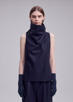 A person with straight brown hair wears the ISSEY MIYAKE SHELL sleeveless jersey top, paired with black pants and black gloves, standing against a plain light gray background in signature ISSEY MIYAKE style.