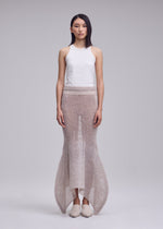 A person faces forward, wearing a sleeveless white top and the ISSEY MIYAKE PANINI PULLED knit skirt—long, sheer, textured with a flared hem—against a plain light gray background.