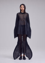 A person stands facing forward, wearing the ISSEY MIYAKE PANINI PULLED—a sheer black knit top with wide sleeves and flared, mermaid-like pant legs—against a plain light gray background.