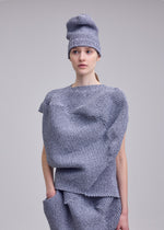 A person models the ISSEY MIYAKE FOUND STONE textured, stone-inspired knit top with sculptural shapes and a matching hat, posing against a plain light gray background.